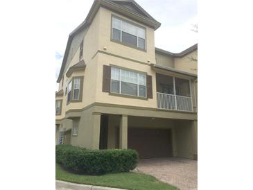 Tan three-story townhome with brown garage door, balcony, and landscaping at 2586 Grand Central Pkwy # 1, Orlando, FL 32839