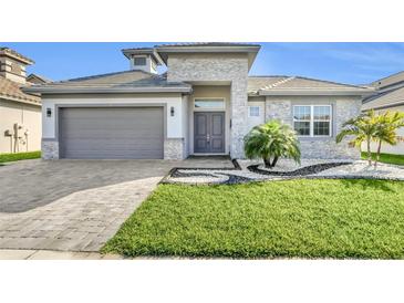 Beautiful single-Gathering home with a manicured lawn and a gray stone exterior and matching garage door at 247 Hampton Loop, Davenport, FL 33837
