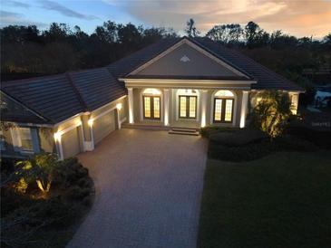Stunning home exterior featuring lush landscaping, red tile roof, brick driveway, and illuminated entryway columns at 6533 Cartmel Ln, Windermere, FL 34786