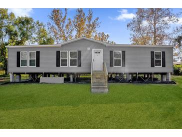 Gray manufactured home with wooden steps and a grassy lawn at 1356 Cupid Ave, Christmas, FL 32709