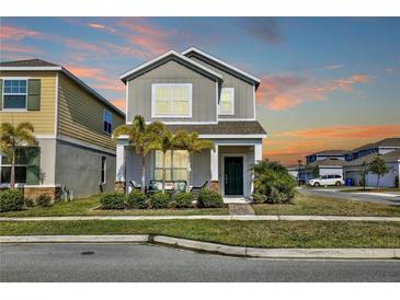 A gray two-story home with manicured lawn, green door, and small front porch with seating at 2429 Volunteer Ave, Kissimmee, FL 34744
