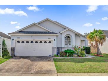 One-story house with a white exterior, two-car garage, and landscaped front yard at 104 Sunny Oak Trl, Kissimmee, FL 34746