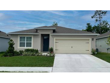 One-story home with beige exterior, a two-car garage, and well-manicured lawn at 2148 Pigeon Plum Dr, Haines City, FL 33844