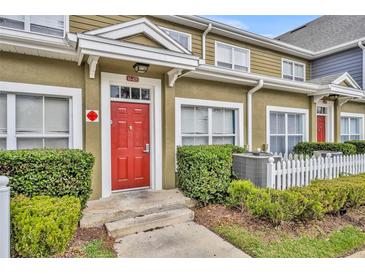 Charming townhome entrance featuring a vibrant red door, lush landscaping, and a white picket fence at 2602 Lodi Cir # 105, Kissimmee, FL 34746