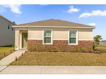 Inviting single-Gathering home featuring decorative stone accents, green door, and manicured front lawn at 6895 Botanic Blvd, Harmony, FL 34773