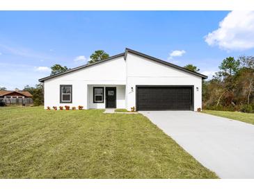 Modern one-story white house with a black door and black two car garage, sitting on a green lawn at 2956 Sw 162Nd Street Rd, Ocala, FL 34473