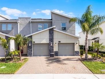 Contemporary two-story townhome featuring a brick driveway, attached garages, and lush landscaping with mature palm trees at 635 Ocean Course Ave # 635, Champions Gate, FL 33896