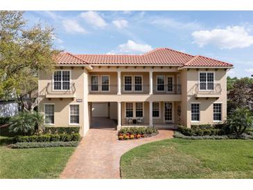 Elegant two-story home with a red tile roof, balcony, brick driveway, and well-maintained landscaping at 8424 Lake Burden Cir, Windermere, FL 34786