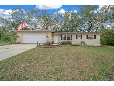 Charming single-story home with a well-maintained lawn, attached garage, and an American flag at 212 Glenn St, Leesburg, FL 34748