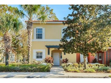 Charming yellow two-story townhouse featuring a well-maintained front yard with lush greenery and palm trees at 8452 Crystal Cove Loop, Kissimmee, FL 34747