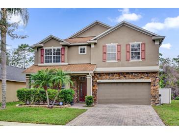 Charming two-story home with stone accents, red shutters, landscaped yard, and a brick paver driveway at 1555 Lalique Ln, Orlando, FL 32828