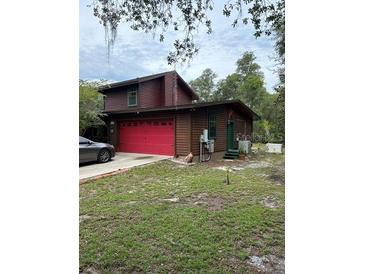 Charming log cabin style home features a red garage door and verdant lawn at 40201 Jericho Trl, Eustis, FL 32736