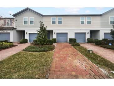 Charming townhomes feature blue garages and red brick driveways, complemented by lush green landscaping and neutral-toned siding at 2033 Milkweed St, Ocoee, FL 34761