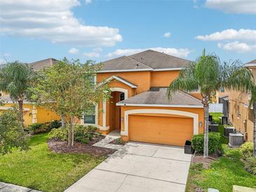 Bright orange two-story home with a two car garage, landscaped front yard, and beautiful palm trees at 2551 Dharma Cir, Kissimmee, FL 34746