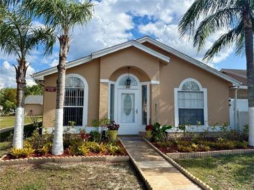 Charming tan home with a well-manicured lawn, tropical plants, and a quaint walkway to the front door at 281 San Gabriel St, Winter Springs, FL 32708