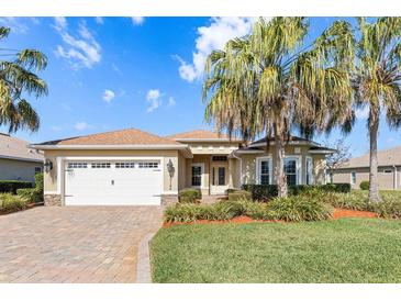 Charming single-story home showcasing a well-manicured lawn, palm trees, and a brick driveway leading to a two-car garage at 10144 Lake Miona Way, Oxford, FL 34484