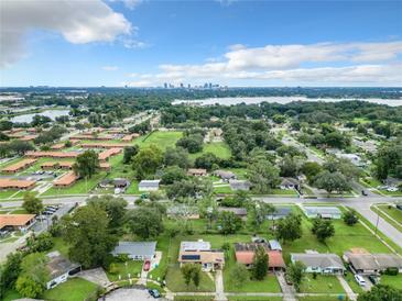 An aerial view shows a neighborhood with a lake, trees, and a distant city skyline under a blue, partly cloudy sky at 23 Judith Ln, Orlando, FL 32811