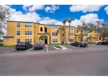 Low-angle view of a yellow two-story apartment building with ample parking and palm trees in the landscaping at 4536 Commander Dr # 1537, Orlando, FL 32822