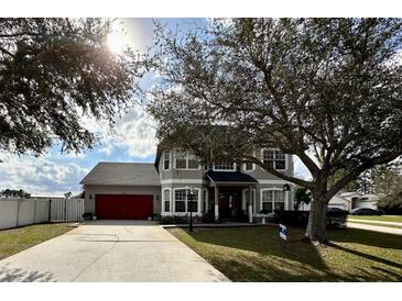 Charming two-story home with a well-manicured lawn, mature landscaping, and a red two-car garage door at 546 Nogales Ct, Kissimmee, FL 34758