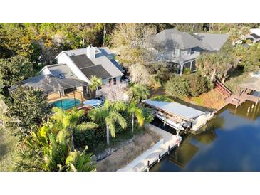 Waterfront home featuring a screened-in pool, boat lift, and lush tropical landscaping at 124 Godfrey Rd, Edgewater, FL 32141
