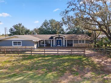 Charming home with a light blue facade, stone accents, a wooden fence, and mature shade trees at 37224 Apiary Rd, Grand Island, FL 32735