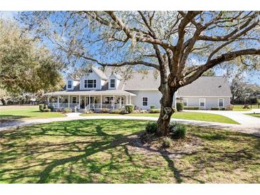 Charming light grey home featuring a large wrap-around porch and mature shade trees at 5150 Banana Point Dr, Okahumpka, FL 34762