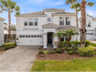 Charming two-story home with a manicured front yard and a two-car garage, enhanced by lush landscaping and tall palm trees at 1440 Pro Shop Ct, Davenport, FL 33896