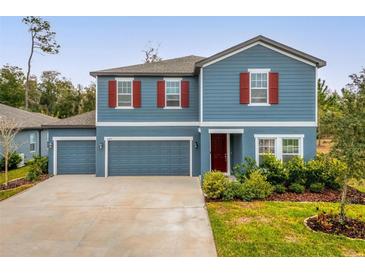 Charming two-story blue home featuring red shutters, lush landscaping, and a spacious three car garage at 2067 Buckhanon Trl, Deland, FL 32720