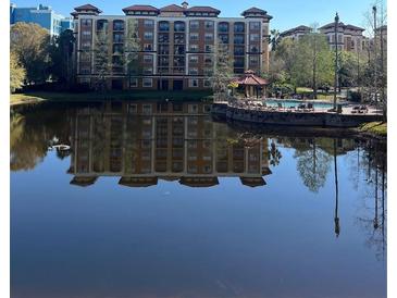 View of a condominium building with a pool and a pond on a sunny day at 12521 Floridays Resort Dr # 206F, Orlando, FL 32821