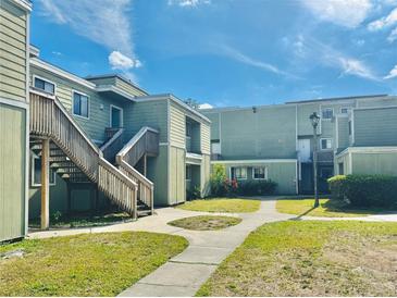 Apartment complex featuring green siding, stairways, and a well-maintained lawn with a walkway on a sunny day at 166 Scottsdale Sq # 166, Winter Park, FL 32792