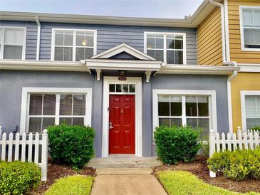 Charming townhome featuring a vibrant red front door, lush landscaping, and a welcoming white picket fence at 2605 Gala S Rd # 103, Kissimmee, FL 34746