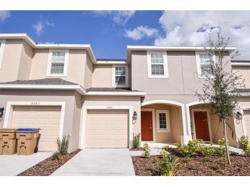 Inviting beige townhome with two-car garage, red door, and neat landscaping at 3587 Davenport Creek Ct, Kissimmee, FL 34746