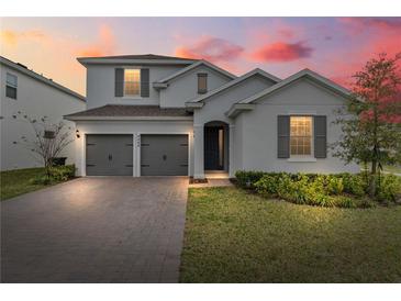 Charming two-story home with gray shutters, a brick driveway, and manicured landscaping at dusk at 4484 Lions Gate Ave, Clermont, FL 34711