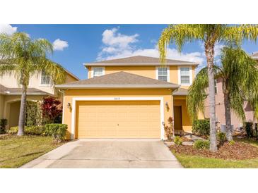Two-story home with a two-car garage, lush landscaping, and vibrant yellow facade at 2613 Santosh Cv, Kissimmee, FL 34746