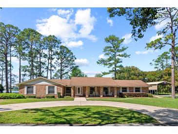 Charming brick home with a circular driveway, manicured lawn, mature trees and rocking chairs on the covered front porch at 5203 Pineview Way, Apopka, FL 32703