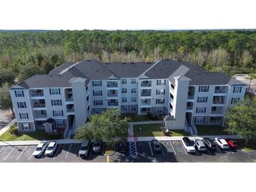 Apartment complex with light blue siding and black shutters, surrounded by green trees, and ample parking at 3176 Feltrim Pl # 205, Kissimmee, FL 34747