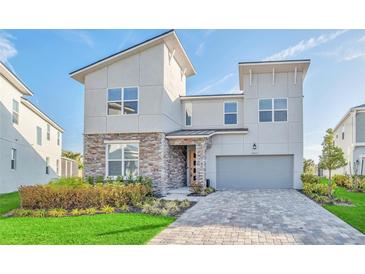 Striking modern home showcasing a stone accent wall, meticulously maintained lawn, and a paved driveway leading to a garage at 8903 Caroline Bay Ct, Kissimmee, FL 34747