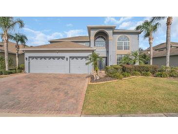 Charming two-story home with a manicured lawn, palm trees, and a brick driveway at 23431 Companero Dr, Sorrento, FL 32776