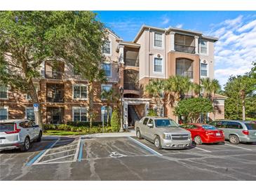 Three-story condo building with multiple balconies, lush trees, and parking, all under a bright blue sky at 1357 Venezia Ct # 402, Davenport, FL 33896