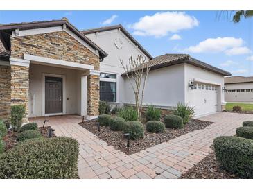 Charming home featuring a stone facade, manicured landscaping, and a welcoming brick walkway leading to the front door at 1407 Deuce Cir, Davenport, FL 33896