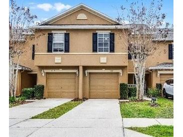 Townhouse with a beige exterior, two stories, black shutters, and two garage doors at 3658 Caruso Pl, Oviedo, FL 32765