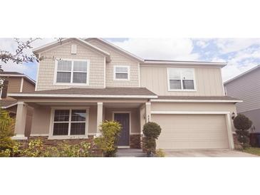 Two-story home with tan siding, stone accents, a covered porch, and an attached two-car garage at 643 Taft Dr, Davenport, FL 33837