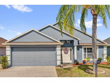 Charming single-story home with a gray two-car garage, complemented by a well-manicured lawn and lush palm tree at 551 Majesty Dr, Davenport, FL 33837