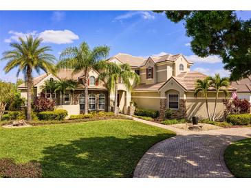 Beautiful two-story home with a well-manicured lawn and lush landscaping, including palm trees and a brick driveway at 11234 Willow Gardens Dr, Windermere, FL 34786