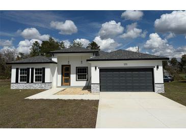 Modern home with a dark gray garage door, stone accents, and a well-maintained lawn at 171 Marion Oaks Trl, Ocala, FL 34473