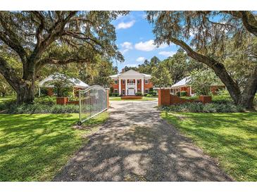 Stately brick home with white columns, gated entrance, and mature trees lining the driveway creating a picturesque view at 2525 Cr 543, Sumterville, FL 33585