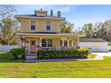 Charming two-story yellow home featuring a welcoming front porch, American flag, and well-manicured landscaping at 2431 Narcissus Ave, Sanford, FL 32771