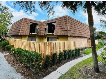 A charming townhome features a wood fence, mature landscaping, and a unique roof design at 5401 Elm Ct # 303, Orlando, FL 32811