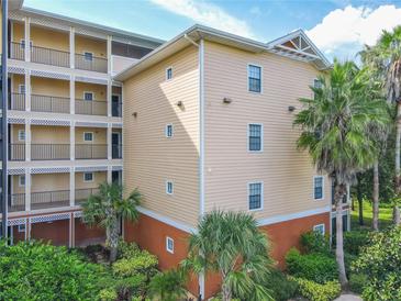 Low-angle view of a peach condo building with multiple balconies and lush landscaping at 3050 Pirates Retreat Ct # 207, Kissimmee, FL 34747