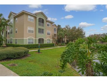 Multi-story condo building with green lawn, lush landscaping, and a view of the pond in a sunny setting at 4865 Cypress Woods Dr # 2105, Orlando, FL 32811